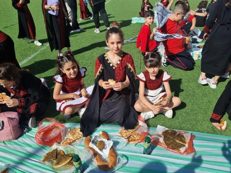 Students in traditional dress share a picnic on the school field