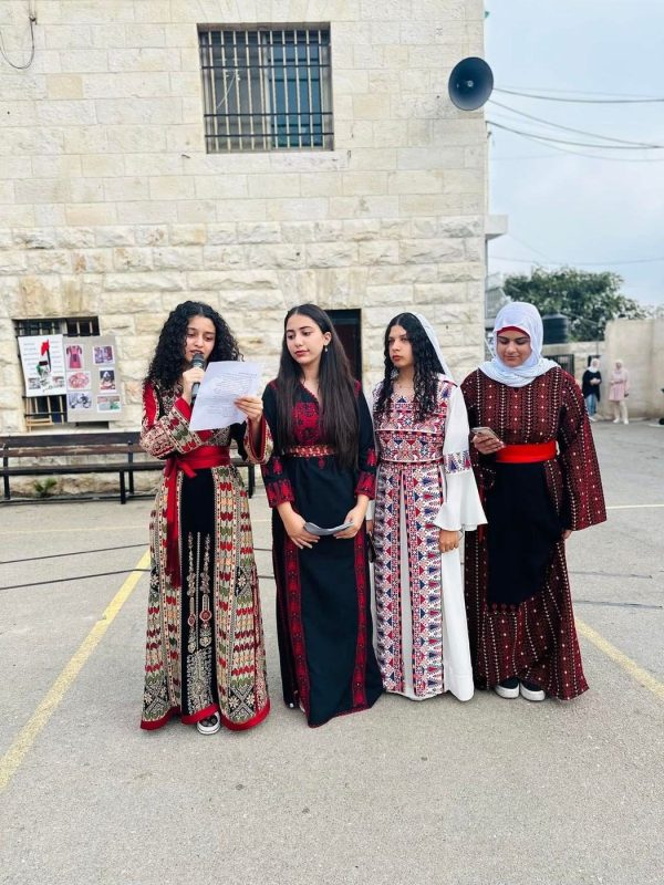 Four students in traditional dresses read a presentation in the courtyard