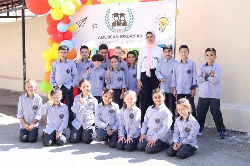 A class and their teacher pose in front of the school welcome banner