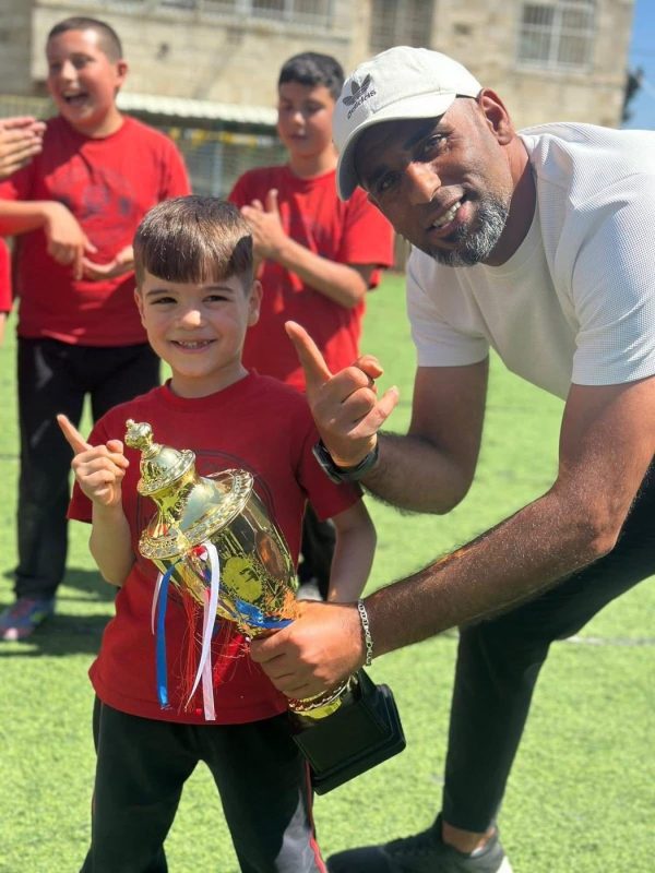 طالب صغير يحمل كأسًا بجانب مدرّبه المبتسم