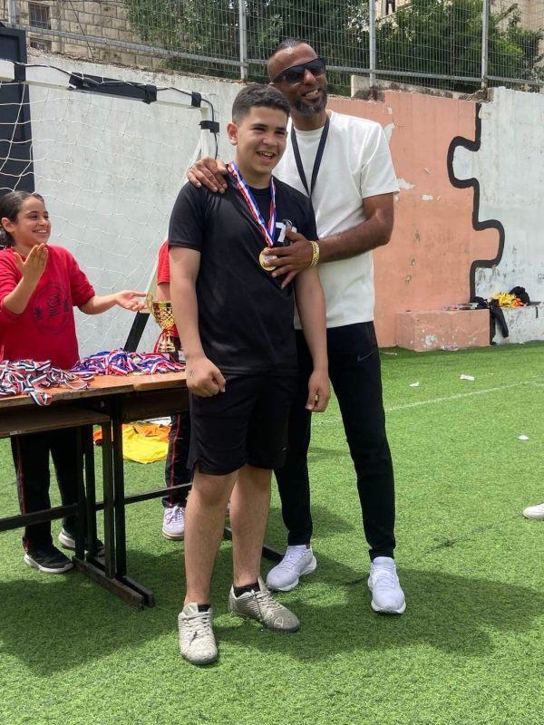 طالب يحمل ميدالية يقف مع مدرّبه في الملعب