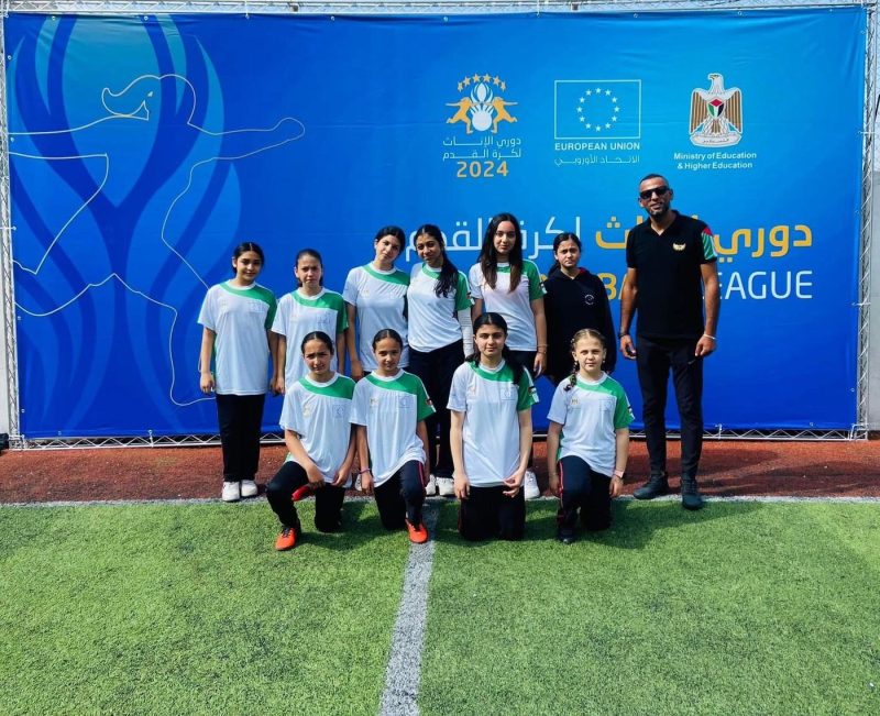 The girls’ football team and their coach pose in front of the 2024 league banner