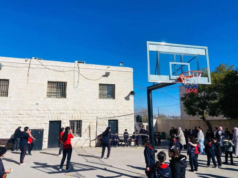 Students in the stone-built school courtyard beside a basketball hoop