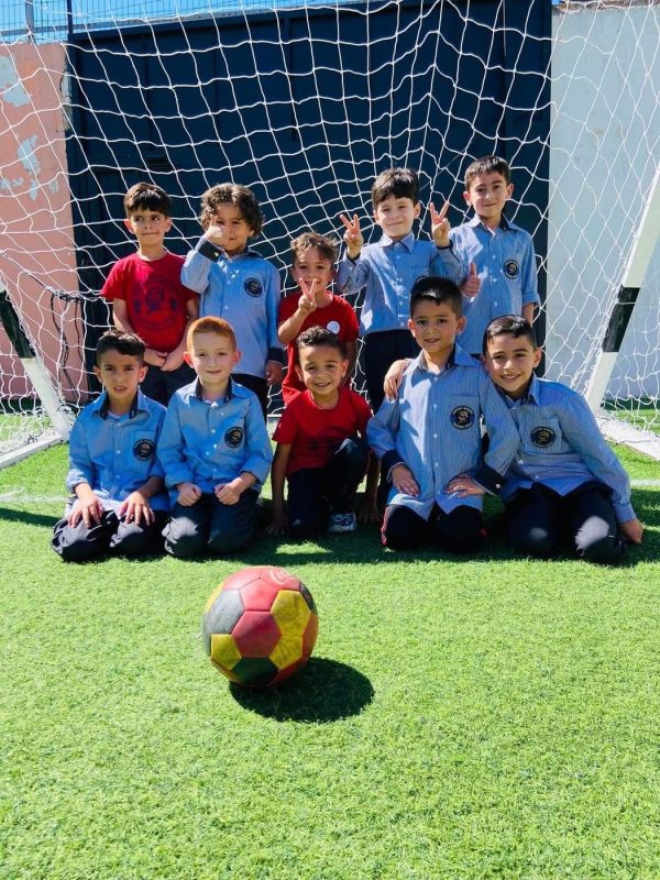 Boys’ football team in front of the goal with a football on the pitch