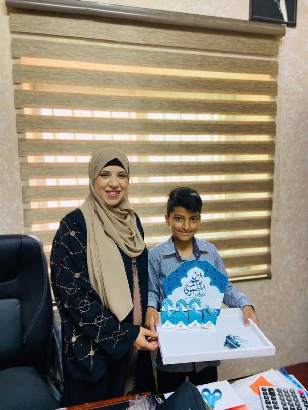 موظفة وطالب يحملان علبة تكريم في مكتب المدرسة