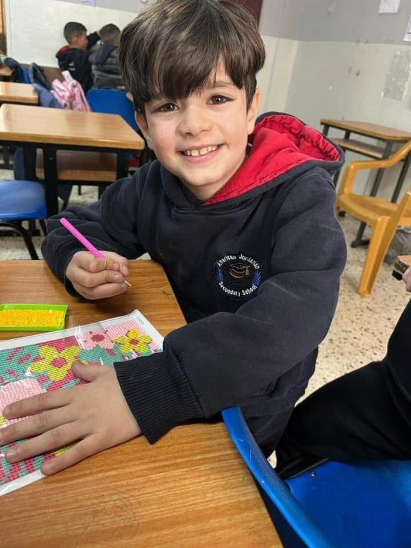 طالب صغير مبتسم يلوّن رسمة على مقعده